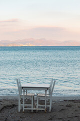 Empty white table and chairs with sea view. Peaceful, nice and romantic place. Vertical photo. No people.