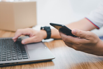 Close up hand a parcel delivery staff hold smartphone check parcel delivery information online and input data in laptop