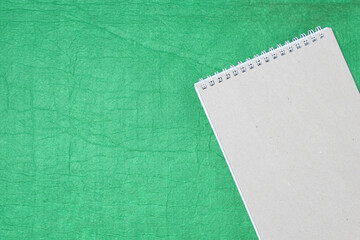 White and gray notepad sheet with spiral against the background of green fabric. Concept of analysis, study, attentive work. Stock photo with empty place for your text and design.