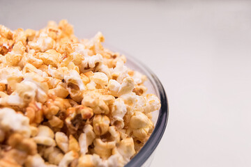 Big transparent glass bowl of freshly popped popcorn on white background