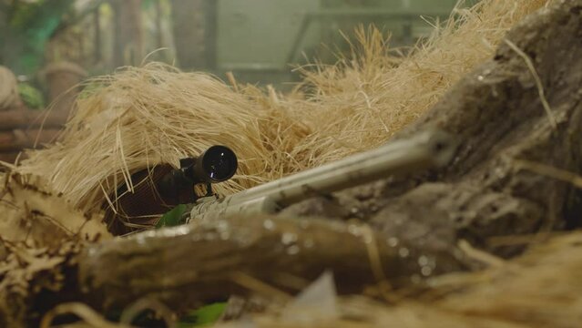 4k Close up view of sniper dressed in ghillie suit or grass cloak waiting and looking by rifle optics . Sharpshooter aims and shoots . Sharp shooter shooting . Shot on ARRI movie camera in Slow Motion