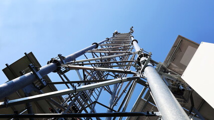 Base station pole metal structure. Steel tower structure of telecommunication base station with transceiver equipment in bottom view with blue sky background. Selective focus