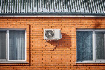 white air conditioner hanging on the brick wall of the building