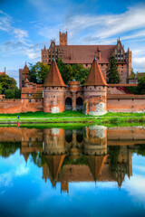 Obraz premium Malbork Castle Reflecting in the River Nogat, Poland, on a Calm Day