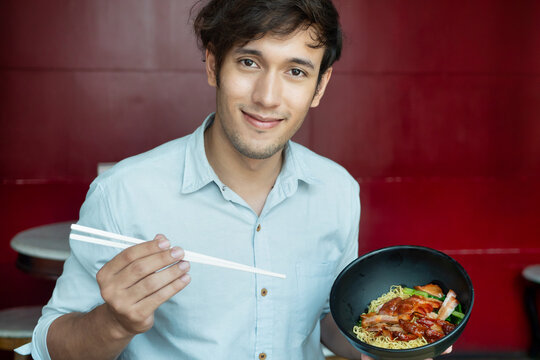 Happy smiling man eating Chinese noodle street food with chopsticks