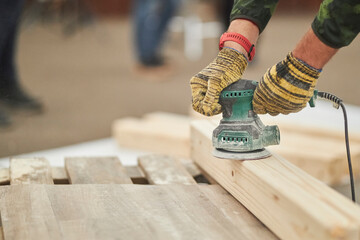 craftsman polishes a solid wood board with a sander, furniture restoration. The polished wood...