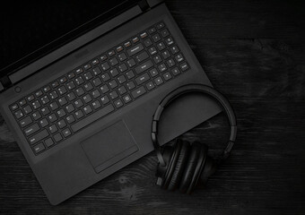 Obraz na płótnie Canvas Gray laptop and headphones with a microphone on a black wooden surface. Distance learning concept in quarantine. Modern freelance. Workplace. Distance communication. Low key photo.