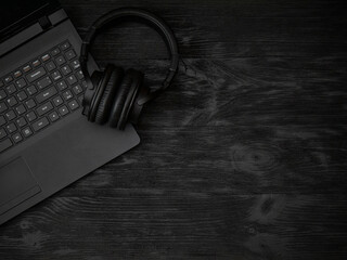 Gray laptop and headphones with a microphone on a black wooden surface. Distance learning concept in quarantine. Modern freelance. Workplace. Distance communication. Low key photo.