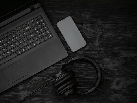 Gray laptop and headphones with a microphone on a black wooden surface. Distance learning concept in quarantine. Modern freelance. Workplace. Distance communication. Low key photo.