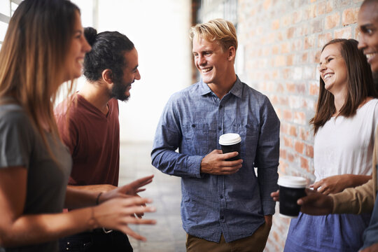 Enjoying A Conversation With Collegues. Shot Of A Diverse Group Of Friends Making Conversation In A Hallway.