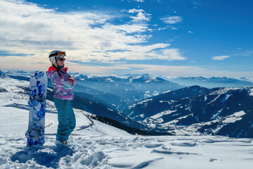 Fototapeta na wymiar A woman posing on powder snow with her snowboard on top of Katschberg in Austria. Panoramic view on the surrounding mountains. Winter wonderland. Sunny winter day. She is full of energy and happy