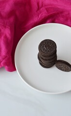 Angle view of chocolate sandwich cookies on a white ceramic plate with fuchsia cloth
