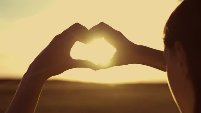 hands forming a heart against the sky. love in the sun. tourist vacation outside. fun girl trip on the weekend. valentine sign at sunset. silhouette young girl dreams love. close-up heart in nature