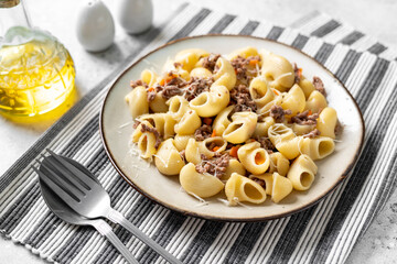 Pasta Pipe Rigate with stew In Bianco in a plate on a gray culinary background. Traditional Italian pasta with ground beef on the kitchen table closeup