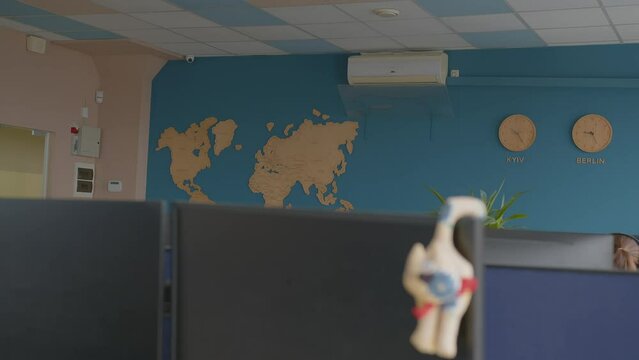 a cartoon cat toy hangs on a monitor in the office. focus transfer to other computers and walls with a wooden world map and kiev and berlin clocks. close-up transfer of focus to the general plan