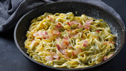 Italian egg pasta carbonara in black pan with bacon, parmesan cheese ,spices and herbs