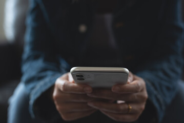 Close up of young woman in blue jeans and sweater using smart mobile phone for online shopping or social media connecting, surfing the internet