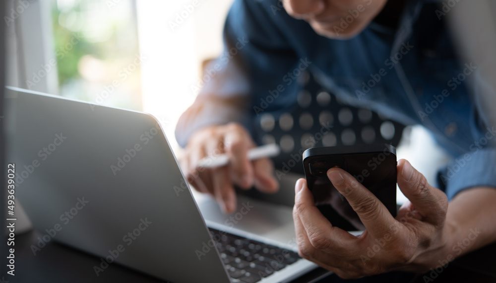 Poster close up of asian casual business man using mobile phone and working on laptop computer with digital