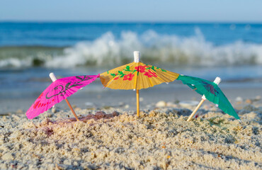 Three small paper cocktail umbrellas stand in sand on sandy beach close-up. Small paper umbrellas...