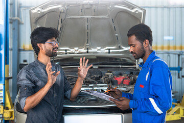 Customer explaining car engine problem while Mechanic noting problems at garage - concept of customer communication, car maintenance service and business conversation.
