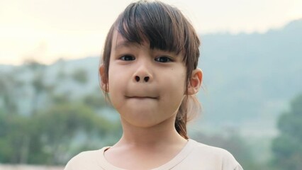 Portrait of a cute Asian preschooler smiling happily in the summer garden. Little Asian child girl showing front teeth with big smile on green nature background. - Powered by Adobe