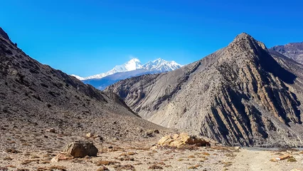 Photo sur Plexiglas Dhaulagiri A panoramic view on dry Himalayan landscape. Located in Mustang region, Annapurna Circuit Trek in Nepal. In the back there is snow capped Dhaulagiri I. Barren and steep slopes. Harsh condition.