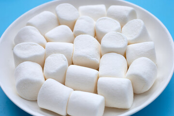 White marshmallows in plate on blue background.