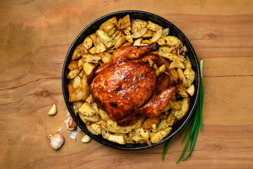 roasted potatoes and baked chicken meat in a frying pan, cooked food, delicious crust, one object on a wooden background