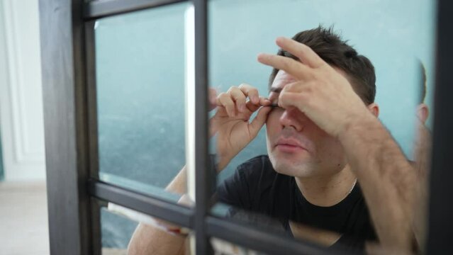 Guy and false eyelashes. A young gay man putting on a false eyelash while putting on makeup before going outside. Close up of Gay applying the false eyelashes looking at the mirror. LGBT conception. T
