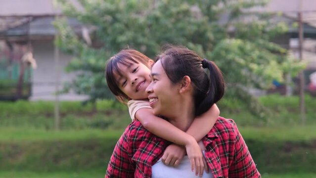 Happy Asian mother holds her daughter in her hands, little daughter raises her hand, imagining herself as a plane in the summer garden.