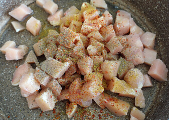 Chicken tenderloin cut into cubes in a pan, topped with pepper, salt, black pepper and dried thyme,