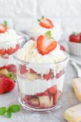 Strawberry tiramisu or trifle, dessert in a glass jar with fresh strawberry and mint leaves on a gray background