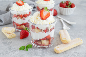 Strawberry tiramisu or trifle, dessert in a glass jar with fresh strawberry and mint leaves on a gray background