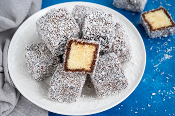 Traditional Australian Lamington cake in chocolate glaze and coconut flakes on a white plate on a...