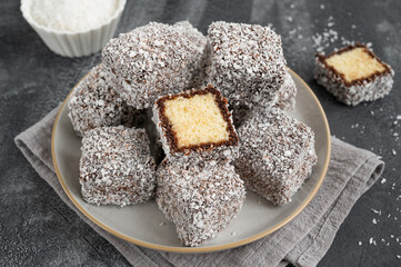 Traditional Australian Lamington cake in chocolate glaze and coconut flakes on a plate on a gray concrete background with a cup of tea. Selective focus.