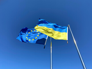 Ukrainian and European Union flags on flagpoles against blue sky