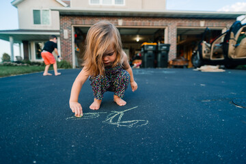 A toddler draws on a driveway with chalk
