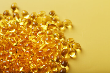 Pile of golden capsules of vitamin D3 on a yellow background with free space