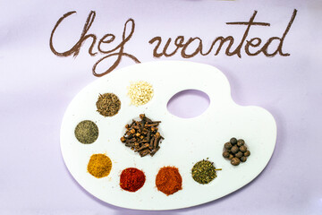 Chef wanted handwritten on purple paper with brown chalk, next to a painter's palette with condiments as painting colors (paprika, curcuma, all spice, cloves, pepper)