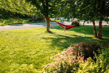 A hammock with a child's leg dangling out of it hangs between two trees
