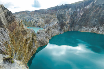 View on the Kelimutu volcanic crater lakes in Flores, Indonesia. Lakes are shining with many shades of turquoise and blue. Sun shines through clouds. Barren and sharp slopes of the volcanic crater © Chris