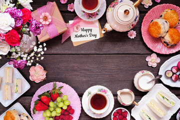 Obraz na płótnie Canvas Mother's Day tea frame over a dark wood banner background. Greeting card, gift, flowers, vintage tea set, finger sandwiches, chocolates, desserts and fruit. Copy space.