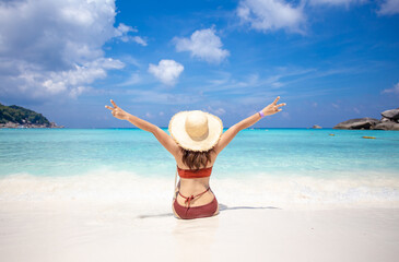 back view of woman wearing a straw hat and orange bikini relax on the beach with beautiful blue...