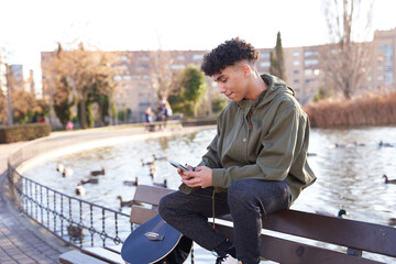 Latino teenager sitting on park bench with smartphone in hand