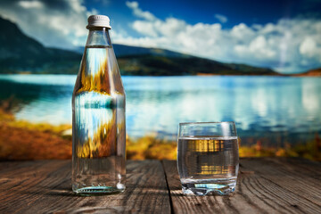 Bottle and glass of water with mountain lake in background
