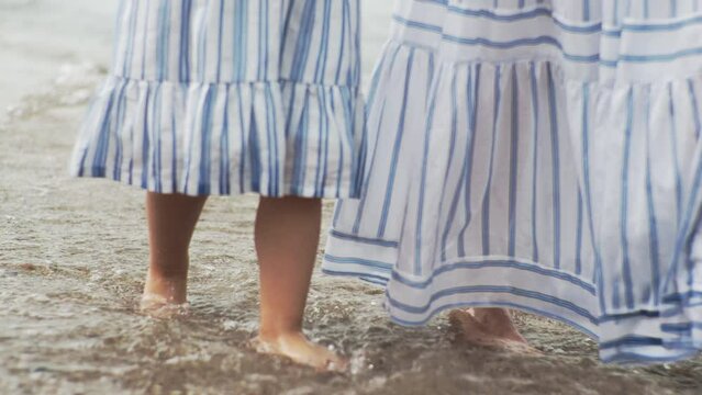 Mother and daughter are walking along the beach on the sand The sea water wet their bare feet