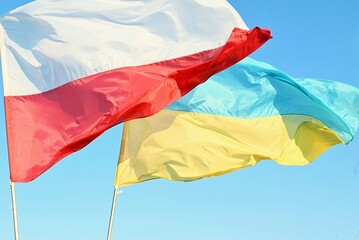 Developing waving  Ukrainian and Polish flags on a blue peaceful sky, support for friendly countries  war in Ukraine
