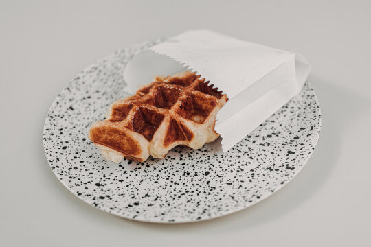 Close Up Of Small Homemade Waffle Served In White Paper Bag.