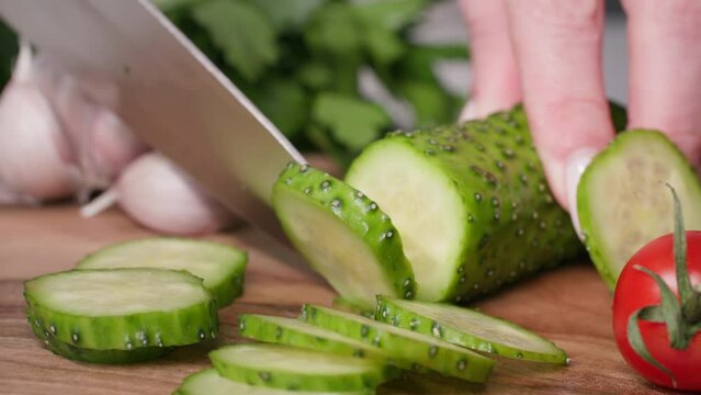food preparation process, female cook cuts fresh cucumber with kitchen knife on cutting dosai to prepare vegetarian dish, close-up