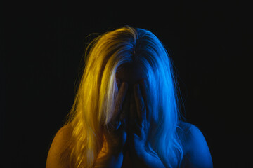 Woman with long hair crying in her hands, illuminated with Ukraine flag colors, yellow and blue,...